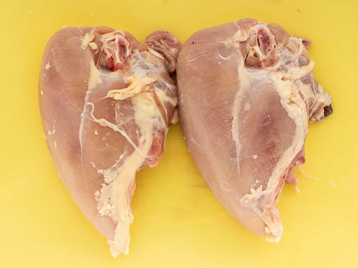 Two split chicken breasts on a cutting board.