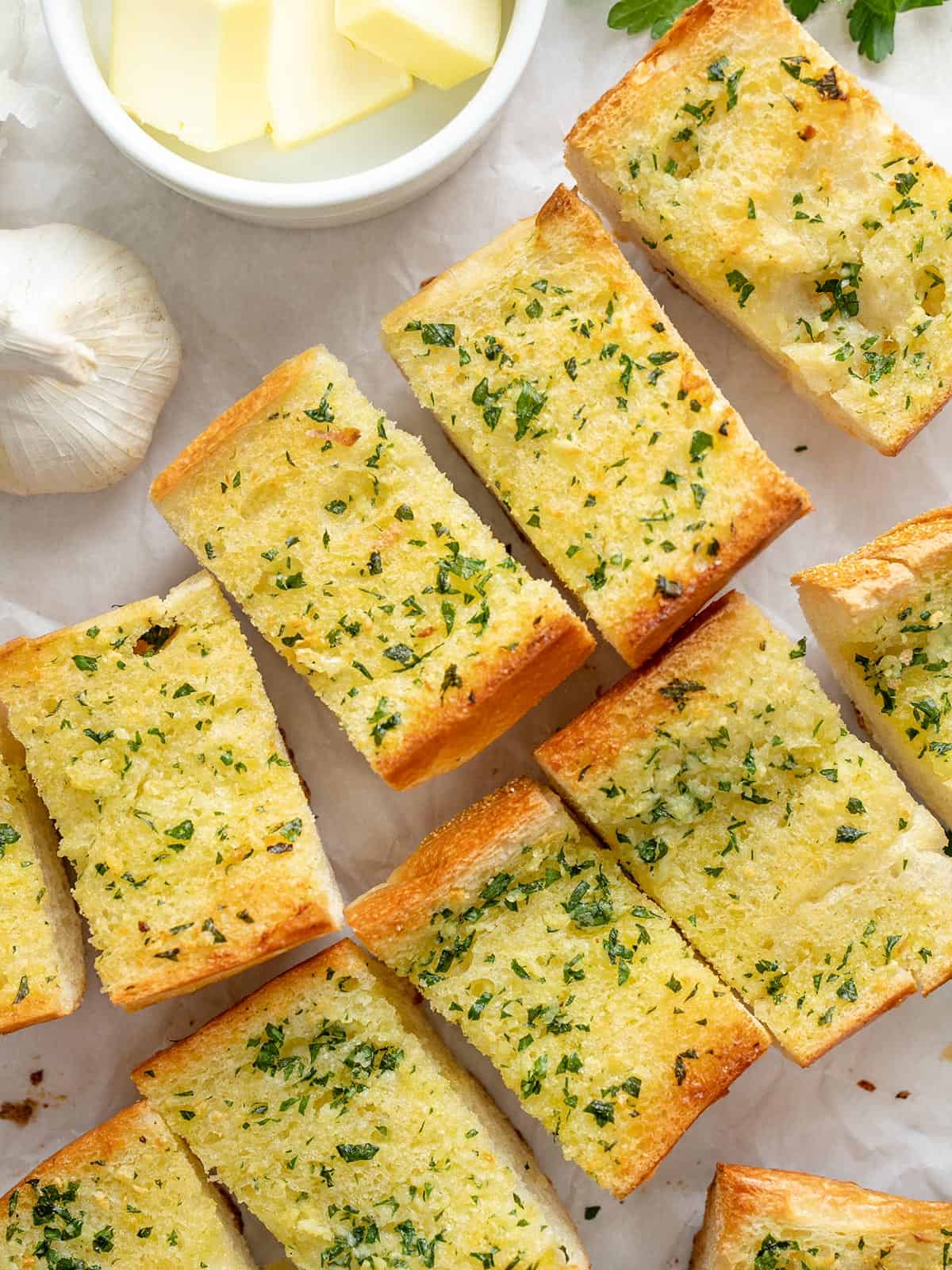 Homemade Garlic Bread is twice as nice for half the price of it's frozen store bought counterpart! An inexpensive and freezer-friendly side dish! BudgetBytes.com Slices of homemade garlic bread on a surface next to a bowl of butter.