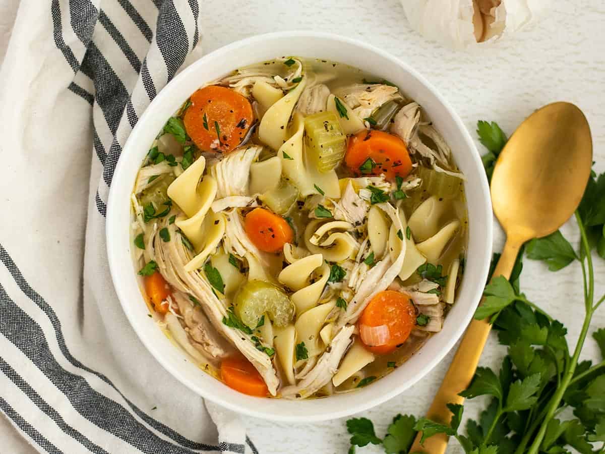 Overhead view of a bowl of chicken noodle soup with a gold spoon on the side.